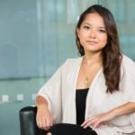 A professional Asian businesswoman sitting confidently in a modern office setting.