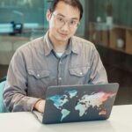 Asian man using colorful map laptop in a modern office setting